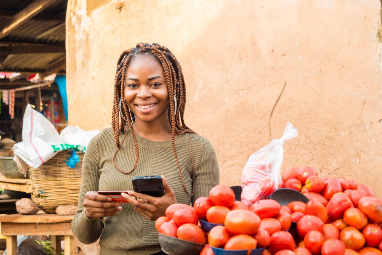 young african woman in a local african market using her mobile phone and credit card